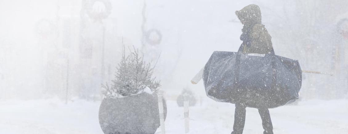 Goalie carrying hockey bag through winter storm